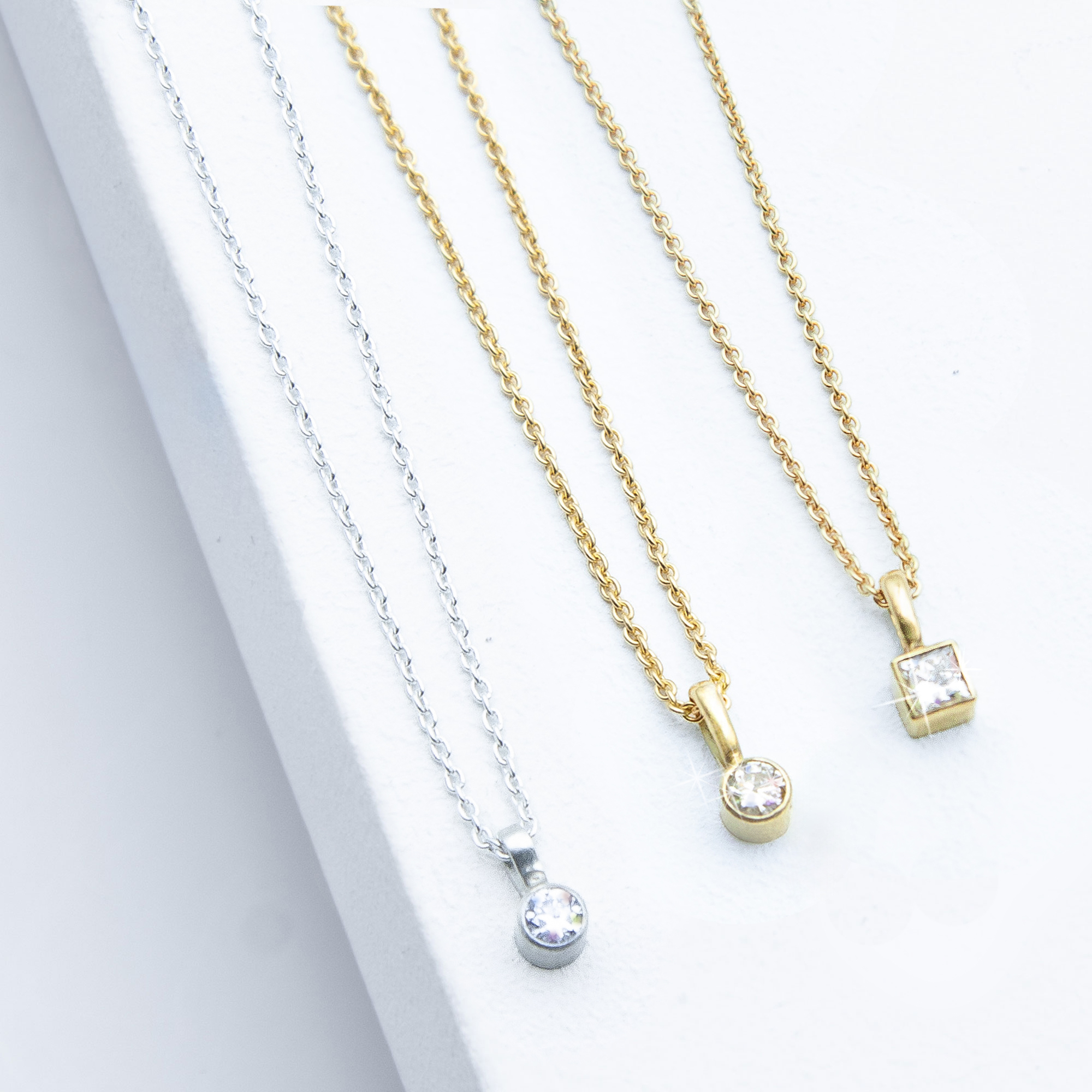 Detailfoto der Sparkle Kollektion von Studio 4L – zwei Diamantketten aus 585er Gelbgold (0,1 ct rund und 0,19 ct carré) und eine Silberkette aus 925er mit 0,1 ct rundem Labordiamant, alle Zargenfassung, 45 cm Ankerkette, 1,1 mm Stärke.